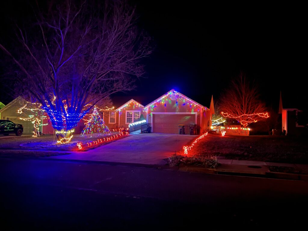 Multicolored lights drip from this house. the driveway is lined in red lights and the tree in the front is covered in blue and white lights.