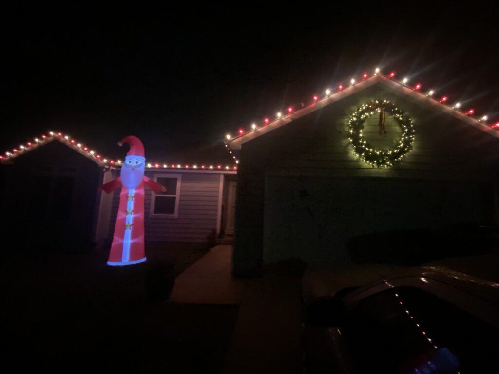 Red and white lights adorn the roof line. A large wreath and an inflatable Santa are in front