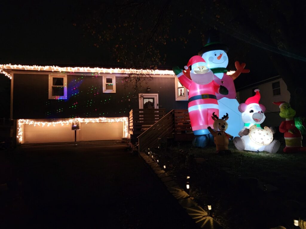 White lights on the roof line with a 20 foot snowman and extra large inflatables sit in front of this house